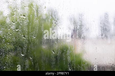 Starker Regen. Regentropfen auf dem Fensterglas an einem Sommertag. Selektiver Fokus, geringe Tiefenschärfe. Wassertropfen fallen auf ein nasses Fenster. Glas voll mit Tropfen während eines Regengusses. Stockfoto