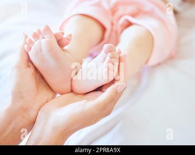 Mutter hält Babyfüße. Nahaufnahme winziger Neugeborenenfüße, die von einem Elternteil gehalten werden. Kleine Babyzehen. Kleines Baby, das auf einem Bett liegt. Eine Frau, die die Füße eines kleinen Mädchens hält. Unschuldiges Kind, das von der Mutter gehalten wird Stockfoto