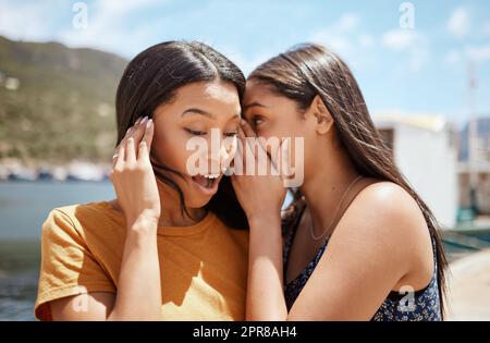 Wahre Freunde verurteilen einander nicht, sie verurteilen andere zusammen. Aufnahme einer jungen Frau, die ihren Freunden ins Ohr flüstert, während sie draußen zusammen abhängt. Stockfoto