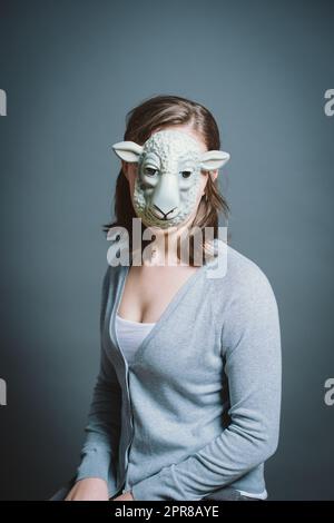 Junge Frau mit Maske vor grauem Hintergrund im Studio. Junge Frau mit Maske vor grauem Hintergrund im Studio. Stockfoto