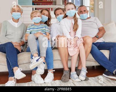 Portrait einer glücklichen Generation, weiße Familie, die Gesichtsmasken trägt, während sie sich zu Hause auf dem Sofa entspannen. Kinder, Eltern und Großeltern bleiben verantwortlich und sicher vor Krankheiten während der Covid-Pandemie Stockfoto