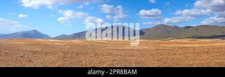 Landschaft geernteter Ackerland an einem bewölkten Tag. Leeres Weizenfeld vor blauem Himmel. Ländliche Landwirtschaft mit trockener Weide in Bergnähe. Breiter Winkel des leeren Schmutzlandes für Hintergrund des Kopierraums. Stockfoto