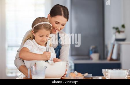 Ich hoffe, es schmeckt so gut wie dein, Mama. Ein entzückendes kleines Mädchen, das ihrer Mutter beim Backen zu Hause hilft. Stockfoto