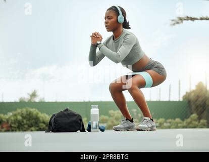 Spüren Sie das Brennen. Ganzkörperaufnahme einer attraktiven jungen Sportlerin, die im Rahmen ihres Trainings auf einem Sportplatz Kniebeugen macht. Stockfoto