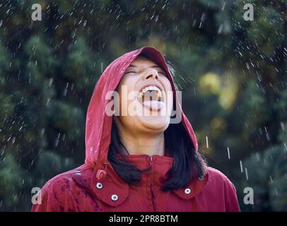 Ohne Regen gibt es keine Regenbögen. Eine junge Frau ragt aus ihrer Zunge, um den Regen draußen zu spüren. Stockfoto