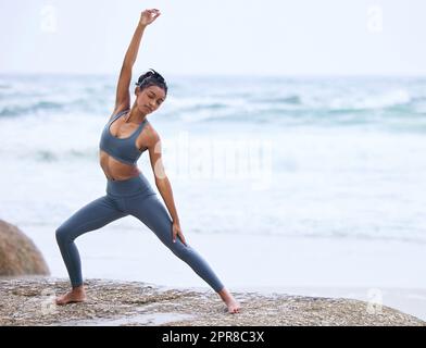 Yoga ist eine Lebensweise. Ganzkörperaufnahme einer attraktiven jungen Frau, die am Strand Yoga praktiziert. Stockfoto