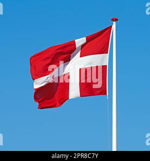 Die dänische Flagge. Die dänische Flagge weht vor blauem Hintergrund. Stockfoto