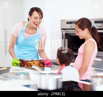 Seelennahrung. Eine aufgeregte Mutter und ihre glücklichen Kinder kochen gemeinsam in der Küche einen Braten. Stockfoto