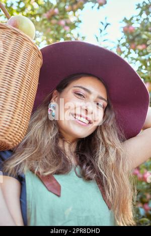 Porträt einer glücklichen Frau, die an sonnigen Tagen einen Korb mit frisch gepflückten Äpfeln von Bäumen auf einer nachhaltigen Obstplantage hielt. Das Gesicht eines fröhlichen Landwirts, der saftige Bio-Früchte in der Saison zum Essen erntet Stockfoto