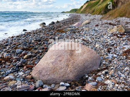 Küste von Kattegat - Helgenaes, Dänemark. Meereswellen, die auf leere Steine am Strand waschten. Ruhiges, friedliches Paradies der Sommerlandschaft und des Himmels für einen entspannten Urlaub im Ausland oder einen Urlaub auf Reisen Stockfoto