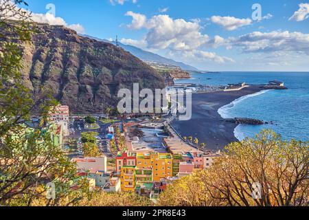 Wunderschöne Meeresküste mit schwarzem Sandstrand auf Puerto de Tazacorte. Farbenfrohe Stadthäuser oder Ferienunterkünfte in der Nähe eines Berges und einer Küste in La Palma, Spanien Stockfoto