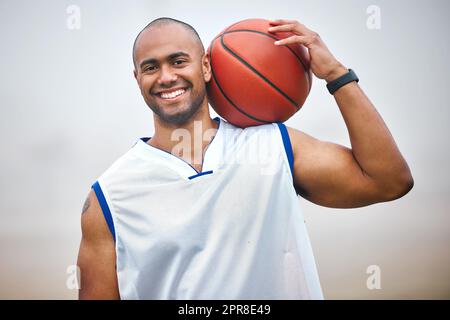 Beim Schießen von Reifen. Beschnittenes Porträt eines hübschen jungen Basketballspielers, der draußen steht. Stockfoto