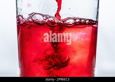 Rote Flüssigkeit in ein Glas gegossen. Weißer Hintergrund. Stockfoto