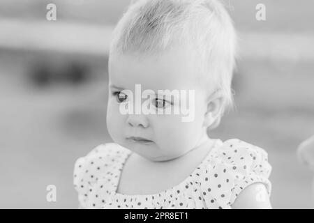 Schwarzweißfoto eines niedlichen Babys in einem Kleid mit Punktmuster Stockfoto