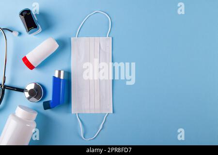 Draufsicht der medizinischen Maske, Stethoskop, Oxymeter, Flasche Pillen und Inhalatoren auf blauem Hintergrund mit Kopierraum. Zum Begriff der inhalativen Schwierigkeitsziffern Stockfoto