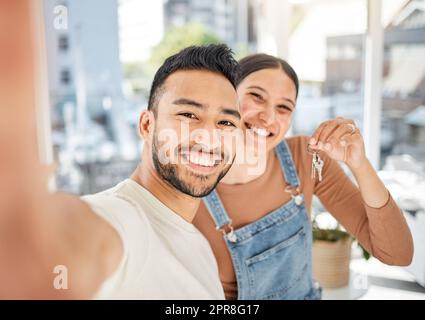 Wir fanden ein schönes Haus in einer schönen Gegend. Porträt eines jungen Paares, das Selfies macht, während es die Schlüssel zu seinem neuen Haus hält. Stockfoto