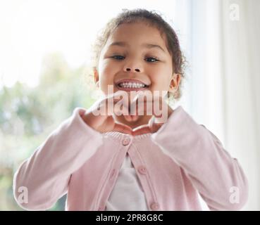 Alles was ich tue ist Liebe zu verbreiten. Aufnahme eines kleinen Mädchens, das mit den Händen zu Hause eine Herzgeste macht. Stockfoto