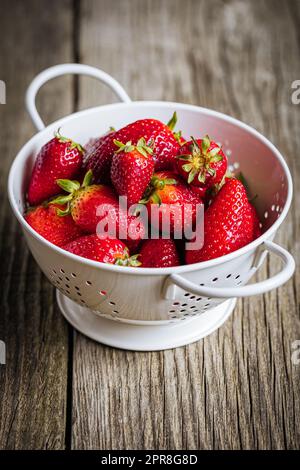 Erdbeeren in weißem Sieb auf rustikalem Holzhintergrund. Frische und leckere saisonale Reife und Früchte. Stockfoto