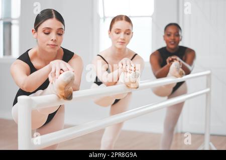 Große Balletttänzer haben ein Talent dafür, Ballett mühelos aussehen zu lassen. Aufnahme einer Gruppe von Balletttänzern, die sich an einer Barre lehnen. Stockfoto