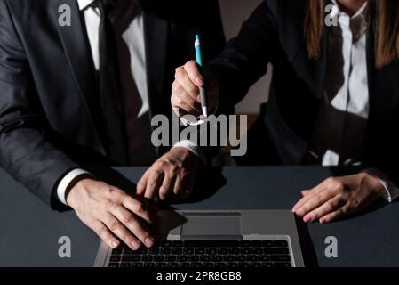 Ein Mann Tippt Auf Dem Laptop Und Eine Frau Zeigt Mit Dem Stift Auf Eine Wichtige Nachricht. Ein Geschäftsmann, Der Über Computer Schreibt, Und Eine Geschäftsfrau, Die Grausame Informationen Präsentiert. Stockfoto