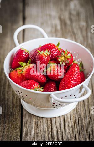 Erdbeeren in weißem Sieb auf rustikalem Holzhintergrund. Frische und leckere saisonale Reife und Früchte. Stockfoto