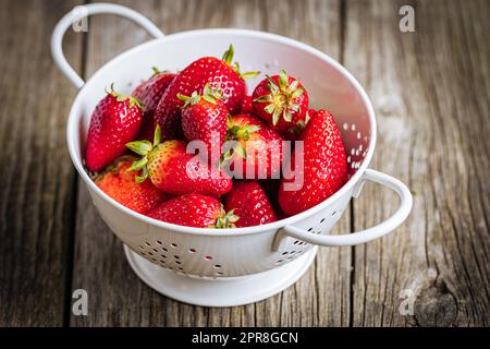 Erdbeeren in weißem Sieb auf rustikalem Holzhintergrund. Frische und leckere saisonale Reife und Früchte. Stockfoto