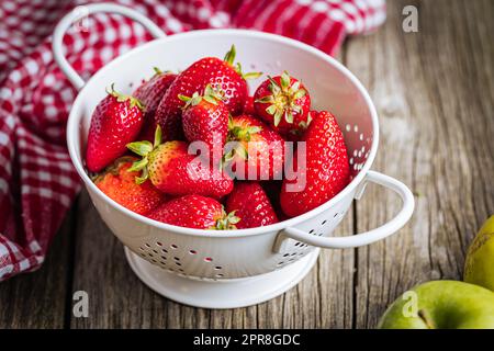 Erdbeeren in weißem Sieb auf rustikalem Holzhintergrund. Frische und leckere saisonale Reife und Früchte. Stockfoto