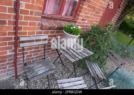 Holzhofstühle und -Tisch in einem privaten Garten mit einer frischen grünen Topfpflanze in Dänemark. Ein ruhiger, friedlicher Hinterhof in Schweden. Entspannen Sie sich im Frühling in einer abgeschiedenen Gegend Stockfoto