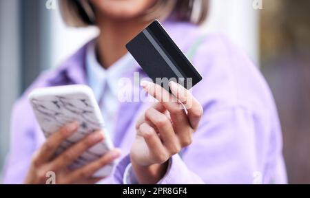 Eine unkenntliche Frau, die ihr Handy und ihre Kreditkarte benutzt, während sie in der Stadt einkaufen. Stockfoto