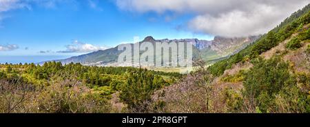 Malerische Berglandschaft in La Palma, Kanarische Inseln, Spanien, vor einem wolkigen blauen Hintergrund mit Copyspace. Wilde Pflanzen und Sträucher wachsen auf einem felsigen Hügel und Klippen in natürlicher Umgebung Stockfoto