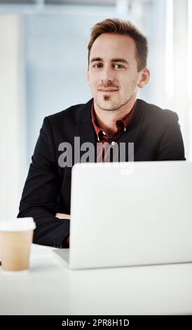 Ich habe hart für die Belohnungen gearbeitet, die ich jetzt ernten kann. Porträt eines jungen Geschäftsmannes, der in einem Büro an einem Laptop arbeitet. Stockfoto