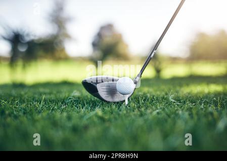 Bereit zum Abschwingen. Nahaufnahme eines Golfballs auf einem Golfkegel mit einem Golfschläger daneben, der ihn tagsüber im Freien treffen würde. Stockfoto