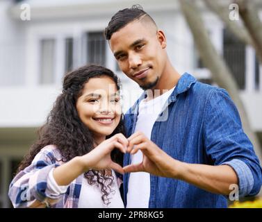 Liebe ist hier, um zu bleiben. Aufnahme eines jungen Paares, das eine Herzgeste mit den Händen im Garten macht. Stockfoto