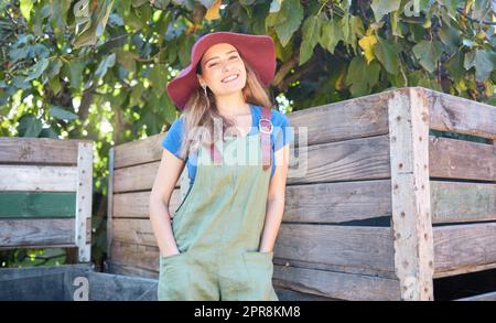 Porträt einer jungen Landwirtin, die an einem sonnigen Tag im Freien Ruhe genießt. Glückliche Frau, die sich entspannt, nachdem sie auf einem nachhaltigen Bauernhof frische Äpfel gepflückt hat, lächelt, entspannt und friedlich auf einem Bio-Obstgarten Stockfoto