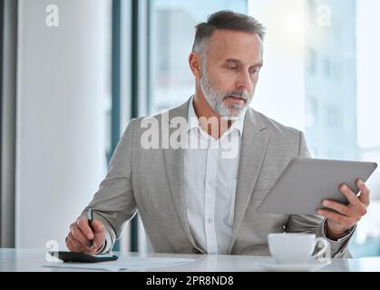 Ein weiser Mensch sollte Geld im Kopf haben. Ein reifer Mann, der ein Tablet und einen Rechner im Büro benutzt. Stockfoto