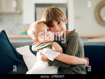 Ein großer Bruder bedeutet, dass du geschützt bist. Zwei kleine Brüder umarmen sich auf der Couch zu Hause. Stockfoto