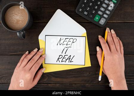 Inspiration mit Schild „Keep IT Real“. Konzeptfoto sei du selbst ehrlich authentisch, authentisch, die Wahrheit sagen immer Frau mit leerem Brief, Kaffee und Schreibwaren auf einem Holztisch. Stockfoto