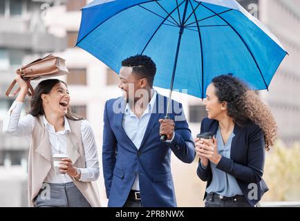 Egal wie der Sturm ist, sie werden immer noch auf Erfolgskurs gehen. Eine Gruppe von Geschäftsleuten, die an einem regnerischen Tag in der Stadt mit einem Regenschirm spazieren. Stockfoto