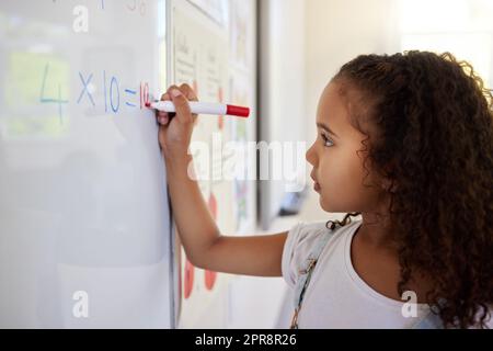 Dies ist einfach die beste Art und Weise für kleine Kinder zu lernen. Ein kleines Mädchen, das Mathematik auf einem Brett in einem Klassenzimmer tut. Stockfoto