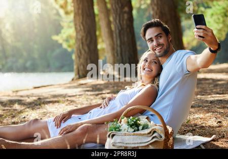 Nehmen wir ein Selfie, um das Datum zu speichern. Ein Paar, das ein Selfie macht, während es im Wald picknickt. Stockfoto