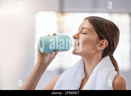 Eine passende junge weiße Frau, die eine Pause macht, um Wasser aus der Flasche zu trinken, während sie im Fitnessstudio trainiert. Sportlerinnen löschen Durst und kühlen sich nach dem Training in einem Fitnesscenter ab Stockfoto