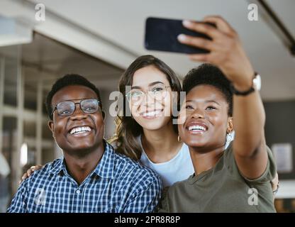 Eine Gruppe junger, fröhlicher Geschäftsleute, die zusammen ein Selfie auf der Arbeit machen. Glückliche afroamerikanische Geschäftsfrau, die mit ihren Kollegen ein Foto auf ihrem Handy in einem Büro macht Stockfoto