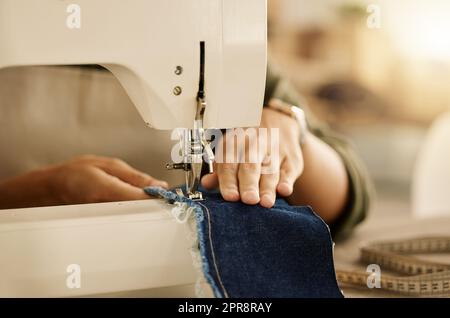 Nahtaufnahme der Hand einer Näherin mit einer Nähmaschine. Modedesigner näht Denim-Stoff an eine Maschine. Schneide ihn mit einer Nähmaschine. Kreativer Unternehmer, der ein Stück Material näht Stockfoto
