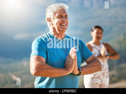 Seniorenmann meditiert mit geschlossenen Händen und geschlossenen Augen tief atmen. Reife Menschen, die Yoga in der Natur machen, leben einen gesunden aktiven Lebensstil im Ruhestand Stockfoto