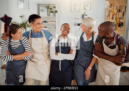 Eine Gruppe von fünf fröhlichen, vielfältigen Bekleidungsdesignern, die in einem Geschäft auf der Arbeit mit gekreuzten Armen stehen. Schneider, die lächeln und lachen, während sie zusammen in einer Boutique stehen Stockfoto