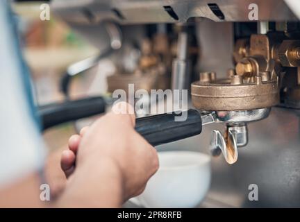 Nahaufnahme eines Baristas mit einem Portafilter während der Zubereitung von gemahlenem Kaffee für einen Shot Espresso für Cappuccino oder Latte in einem Café. Hände des Kellners, der ein warmes Getränk in einem Coffeeshop mit einer Brühmaschine zubereitet Stockfoto