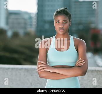 Porträt einer jungen afroamerikanischen Frau, die mit gekreuzten Armen steht, bereit für Sport im Freien. Entschlossene Sportlerin, die fokussiert und motiviert für das Training in der Stadt aussieht Stockfoto