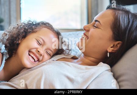 Fröhliche Mutter und kleine Tochter liegen ihren Kopf auf der Brust ihrer Mutter, während sie lachen und Zeit miteinander zu Hause verbringen. Süße Momente zwischen Mutter und Kind Stockfoto