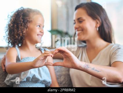 Liebevolle Mutter und liebenswerte Tochter, die zusammen sitzen und eine Herzform bilden, mit ihren Händen auf der Couch zu Hause. Süßer Moment zwischen Mutter und Kind. Mutterschaft ist erfüllend Stockfoto