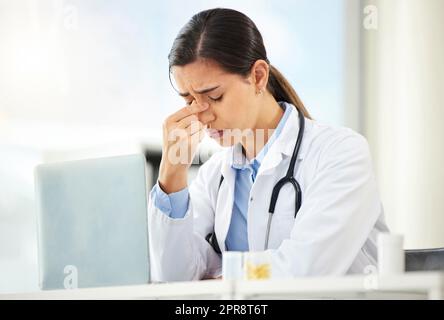 Nahaufnahme einer jungen gemischten Ärztin, die besorgt aussah und Kopfschmerzen hatte, während sie an einem Computer in ihrem Büro arbeitete. Hispanische Frau mit Kopfschmerzen und Stress im Krankenhaus Stockfoto